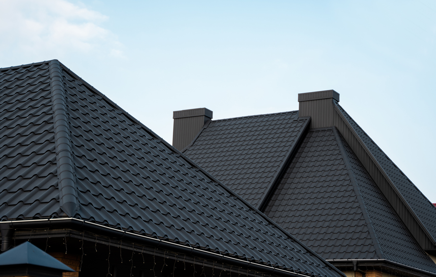 Black metal tile roof. Roof metal sheets. Modern types of roofing materials. Roof of the house, metal roof tile against the blue sky. Building.